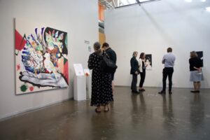 Yleiskuva näyttelytilasta, jossa vierailijoita katsomassa seinälle ripustettuja taideteoksia