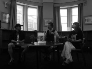 3 ihmiste istuu sohvall aj akeskustelee. Pöydällä sohvan edessä vihko, jonka kannessa lukee Florere