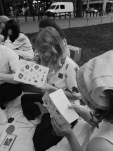 Kolme ihmistä istuu puistossa kesällä ja selailee pieniä kirjoja